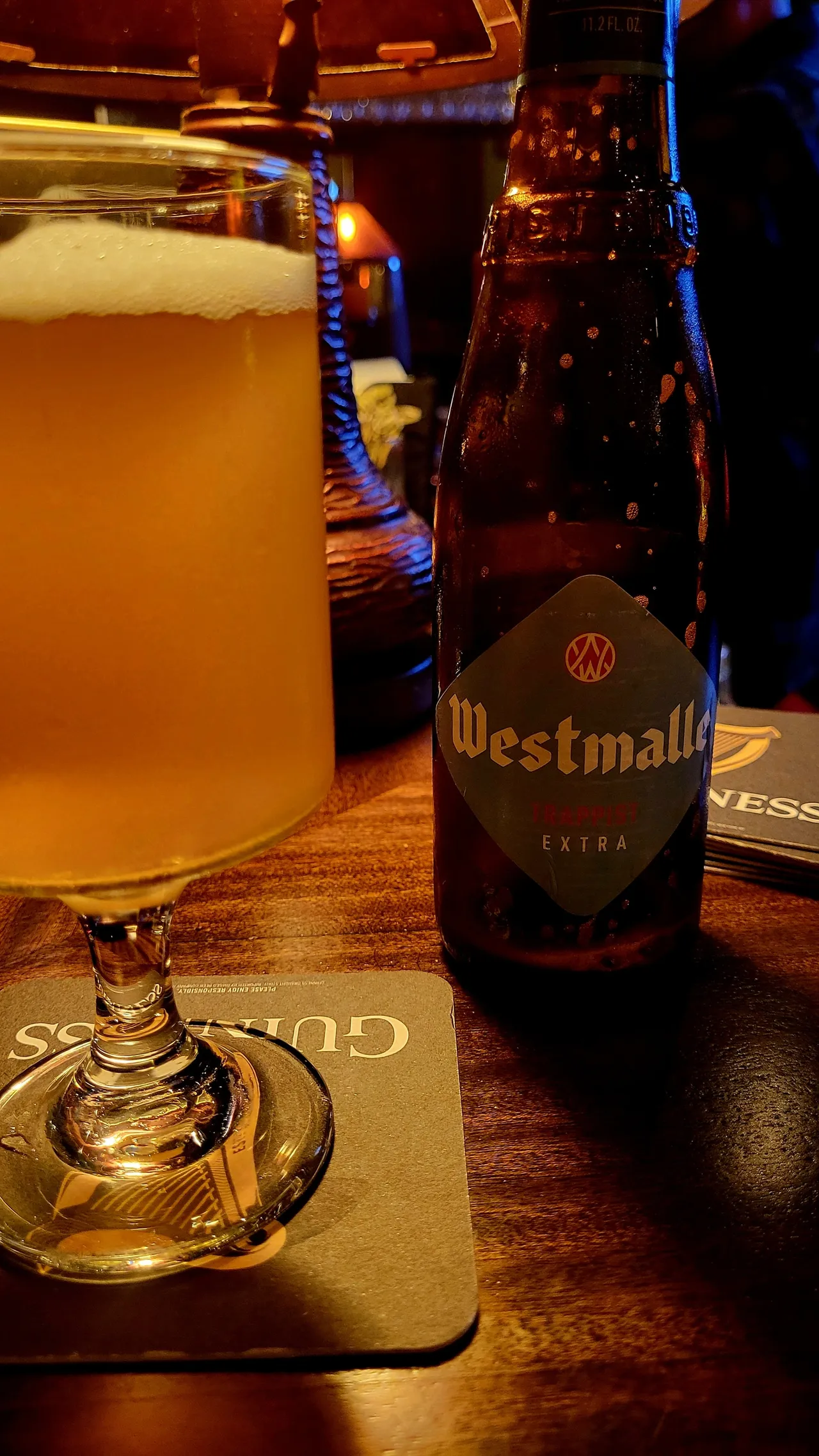 Empty Westmalle beer bottle next to a full stemmed glass