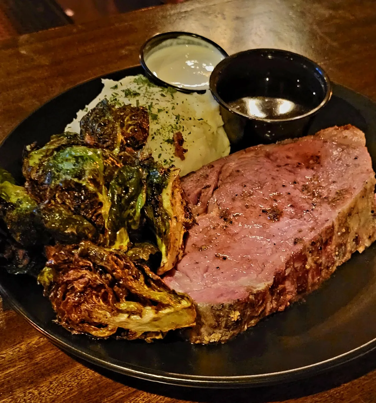 A plate of juicy steak, mashed potatoes, greens and various sauces.