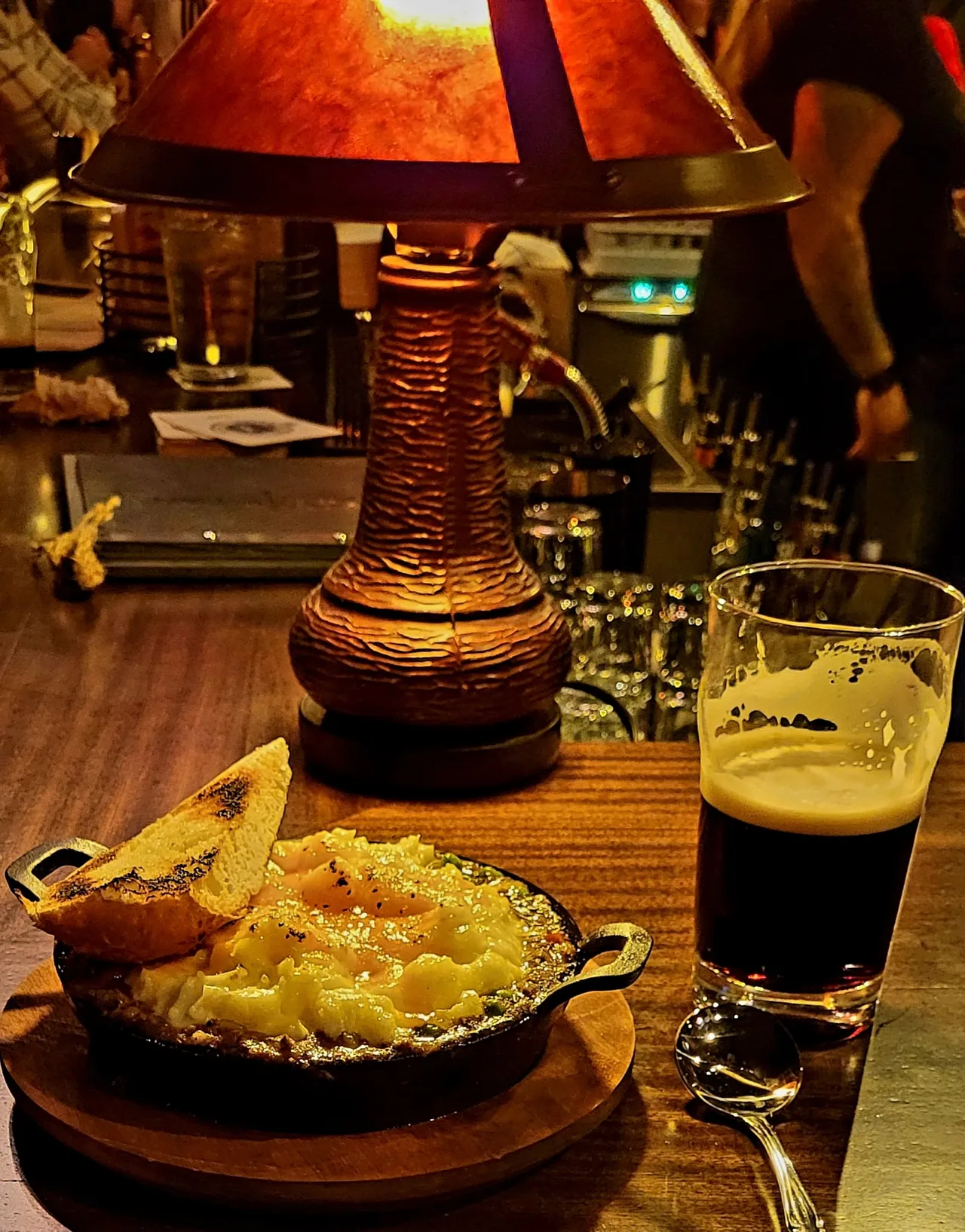 A cast iron skillet with bread and a half full glass of beer.